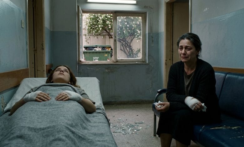 A dimly lit, narrow medical clinic room rendered in muted, desaturated tones of grey and pale blue. In the foreground, a young woman lies on a worn clinic bed, her eyes fixed on the ceiling, her bandaged hands resting motionless on a thin blanket. Beside her, an older woman sits hunched on a shabby sofa, her face pale and hollow-eyed, her own bandaged hands resting in her lap, tears streaming silently down her weathered cheeks. Between them on the floor, scattered shards of broken glass catch the weak fluorescent light. Through a small grimy window in the background, barely visible outside, a large overflowing garbage dumpster sits beneath a jasmine tree, its white blossoms falling softly. The atmosphere is heavy with grief, disconnection, and unspoken generational pain. Cinematic, literary realism style with dramatic chiaroscuro lighting, evoking isolation and emotional devastation.